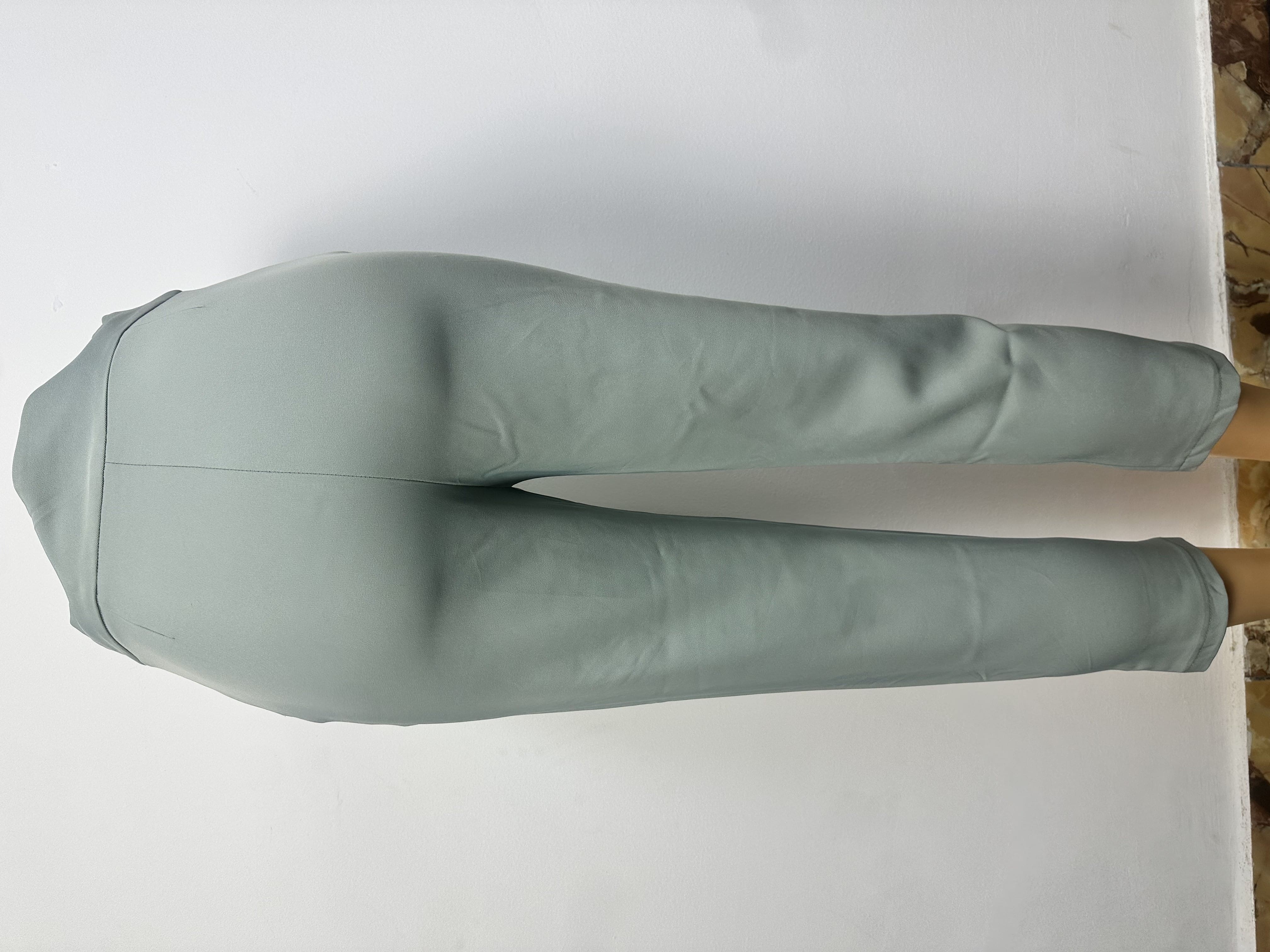 Pantalon est de couleur gris clair uni, à la texture lisse, avec une ceinture ajustée et une couture sur le devant de chaque jambe.