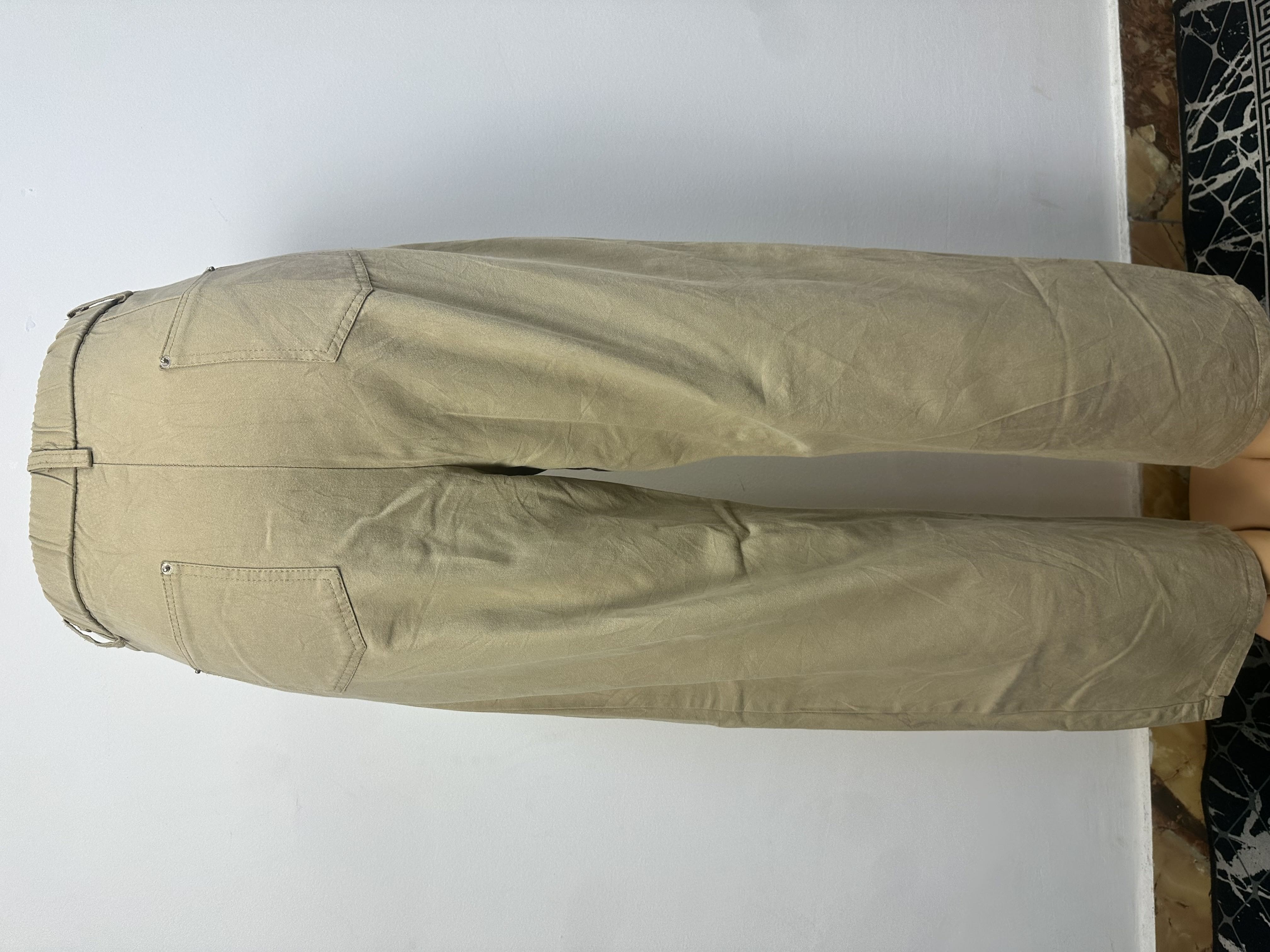 Pantalon beige kaki uni, avec une ceinture ajustée à passants et une fermeture boutonnée. La coupe est droite et ample, coupée au-dessus de la cheville.