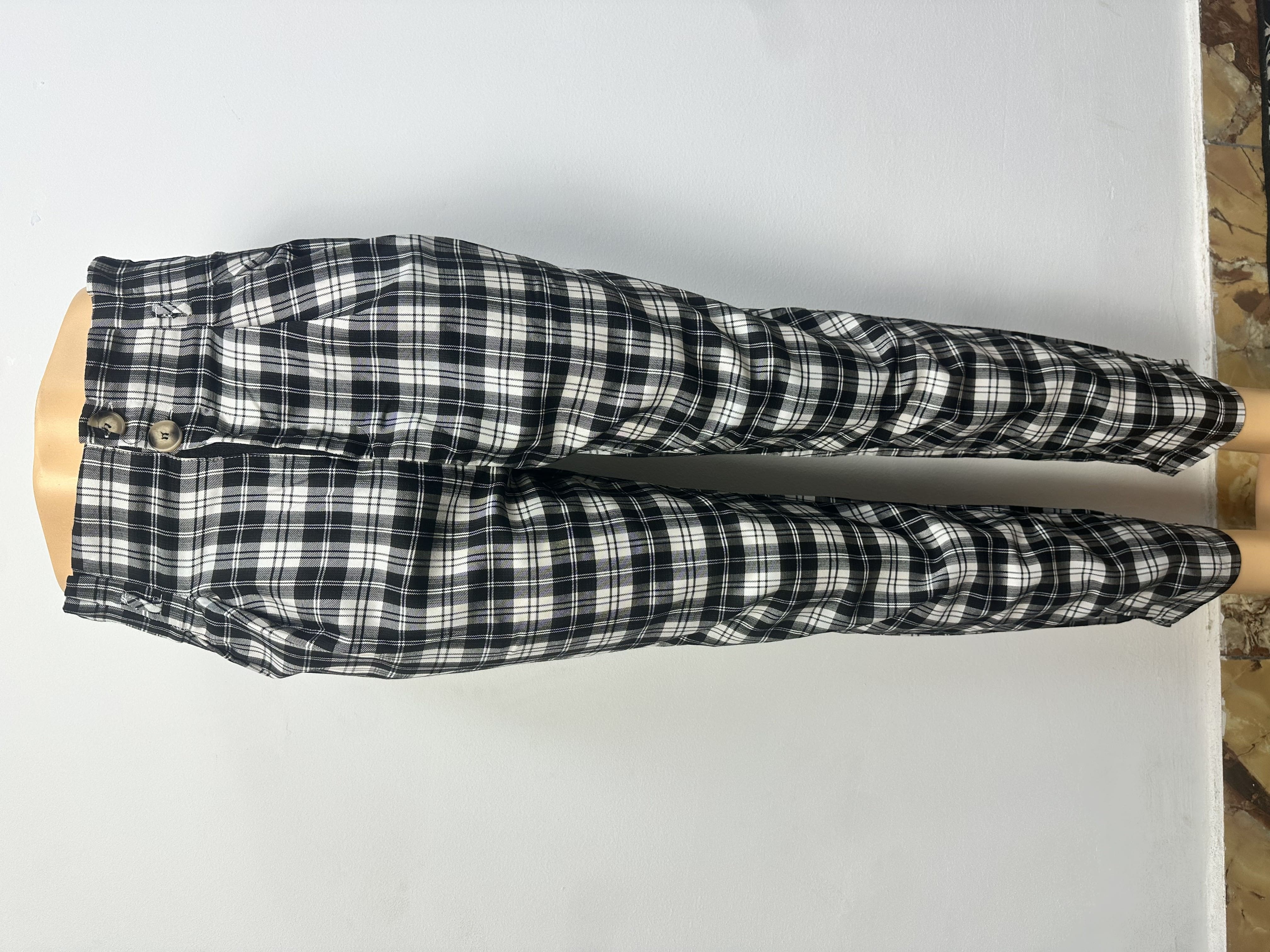 Pantalon à carreaux noirs et blancs, avec une ceinture élastique et deux gros boutons sur le côté gauche.