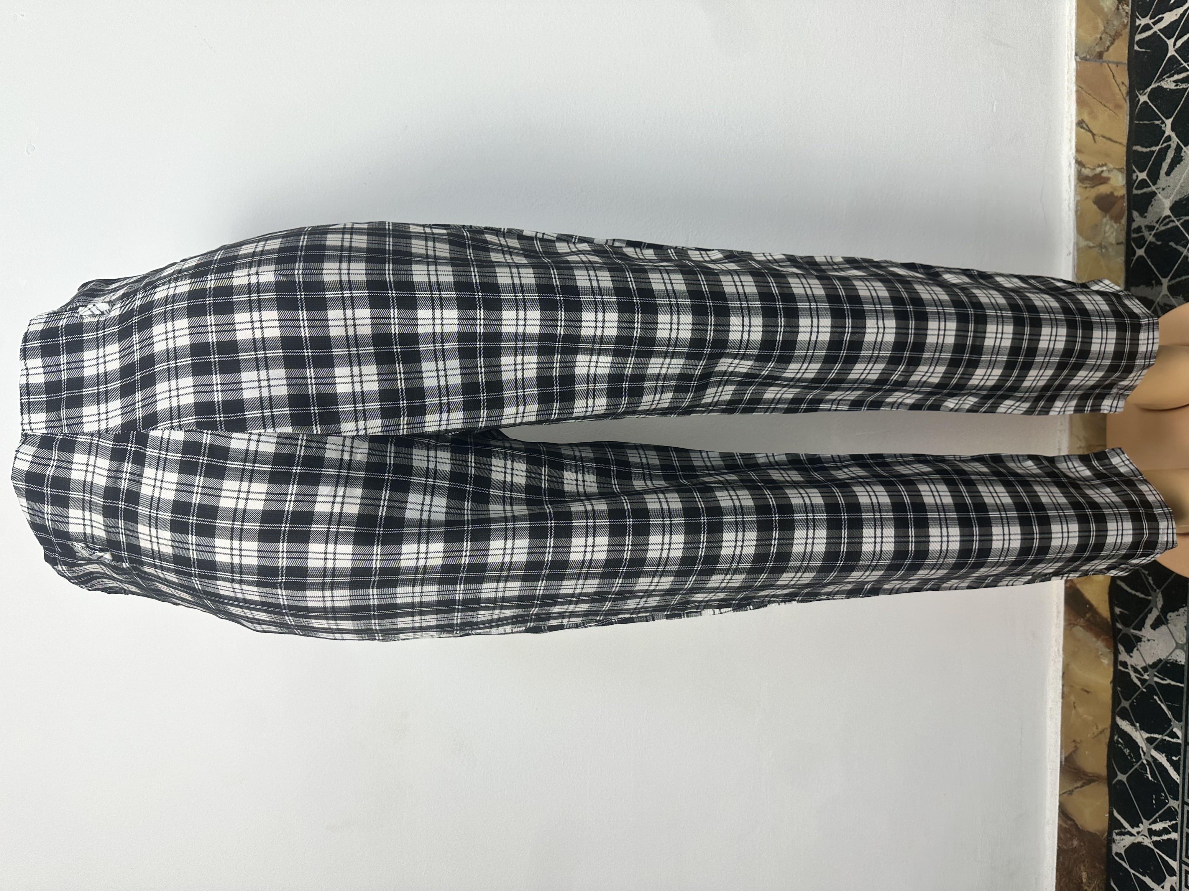 Pantalon à carreaux noirs et blancs, avec une ceinture élastique et deux gros boutons sur le côté gauche.