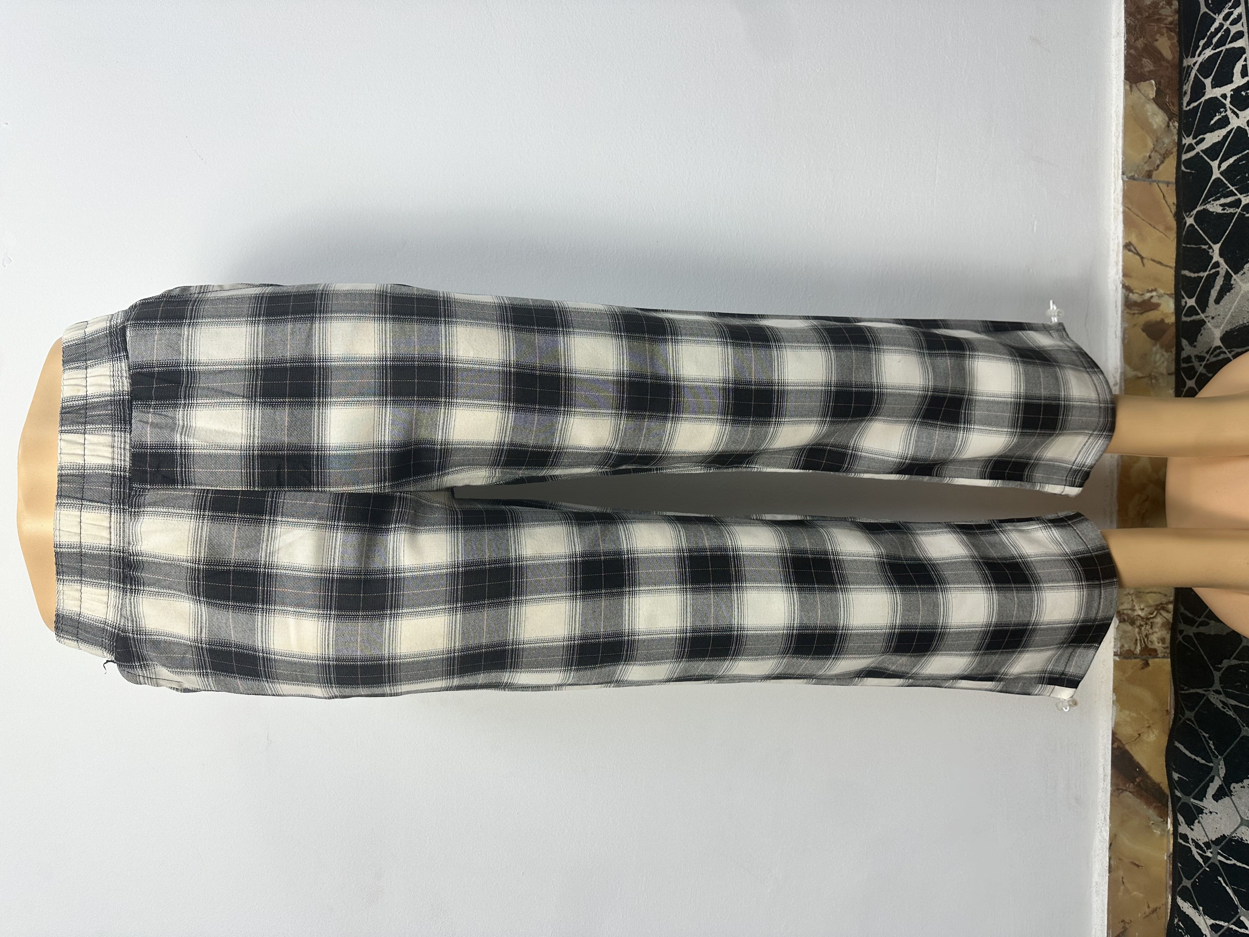 Pantalon à carreaux noir et blanc, avec ceinture élastique, sans boutons ni cordons visibles. Coupe ample et droite, courte au-dessus de la cheville.
