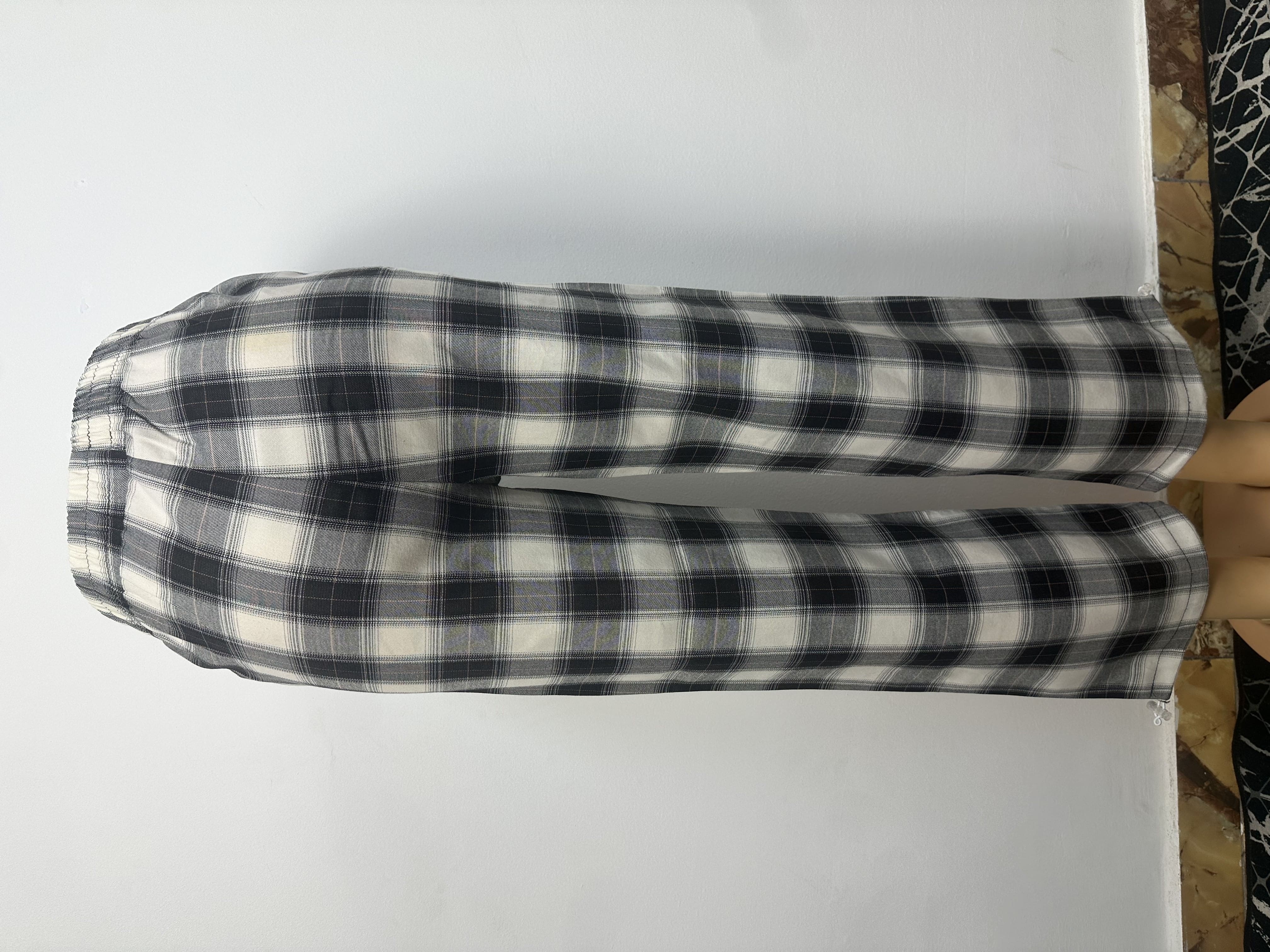 Pantalon à carreaux noir et blanc, avec ceinture élastique, sans boutons ni cordons visibles. Coupe ample et droite, courte au-dessus de la cheville.