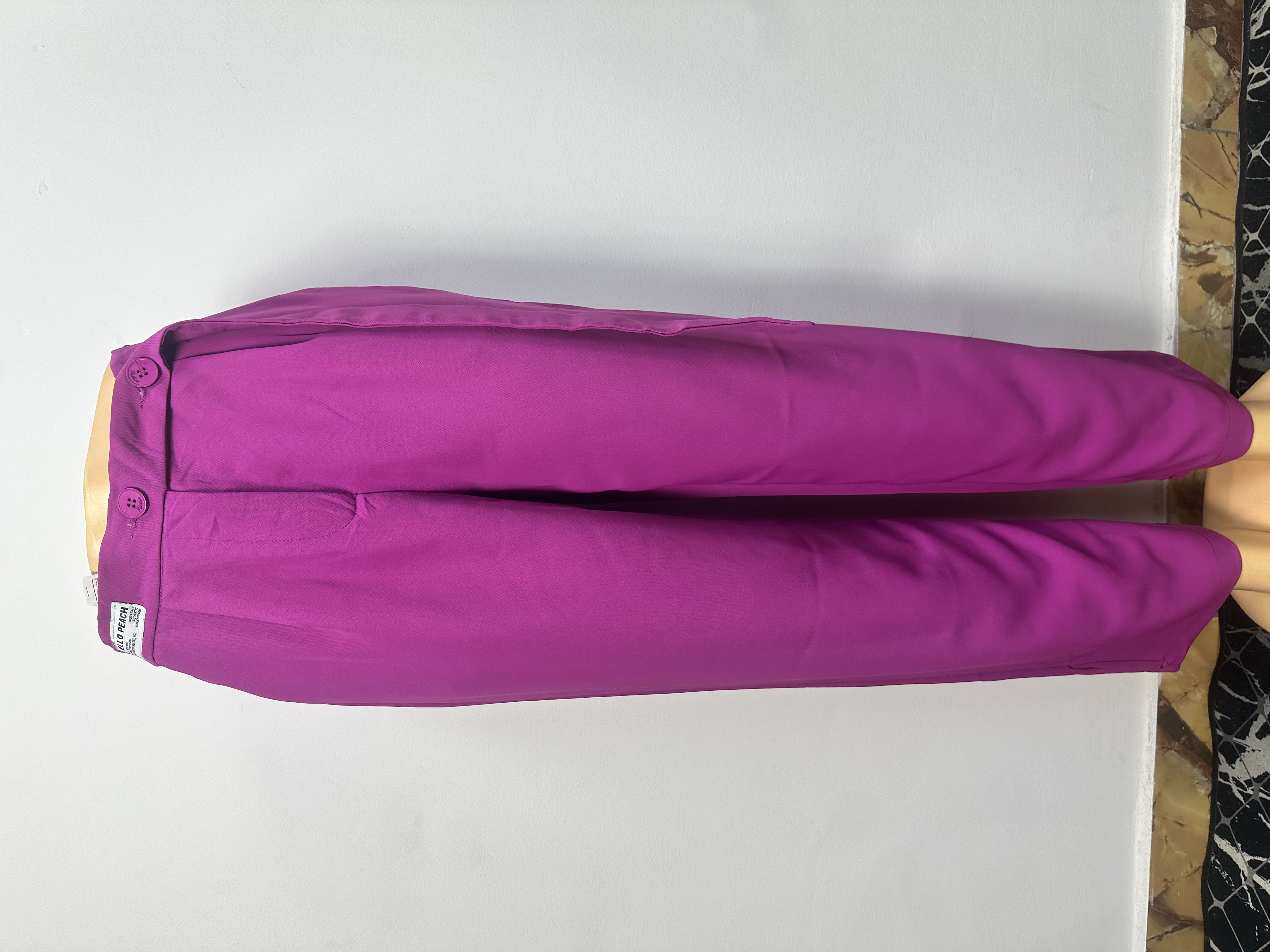 Le pantalon de couleur magenta uni, avec une taille ajustée, des passants, une fermeture à boutons et une petite étiquette blanche sur la ceinture gauche.